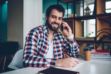 Poz ve telefonla, konuşma yaparken kameraya bakarak mutlu yakışıklı hipster adam portresi smartphone için çağrı kapalı kahve molası sırasında kullanımı ve öğrenimi olumlu erkek öğrenci
