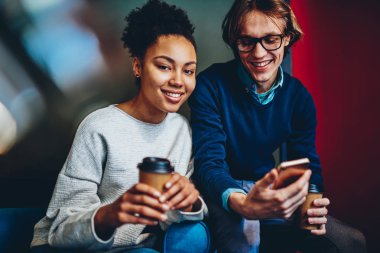 Afrikalı-Amerikalı kadın bakarak onun erkek arkadaşı Gözat web sayfası ise kamera smartphone, çeşitlilik arkadaş ara birlikte cep telefonu kullanımını hipster adam ise harcama.