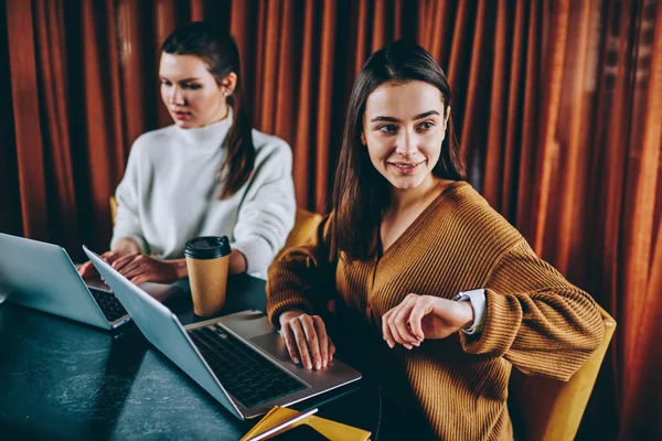 两位成功的女自由职业者远程工作在笔记本电脑设备坐在餐桌上咖啡馆 积极的时髦女孩检查时间和信息的电子 Smartwatch 花时间与朋友 — 图库照片