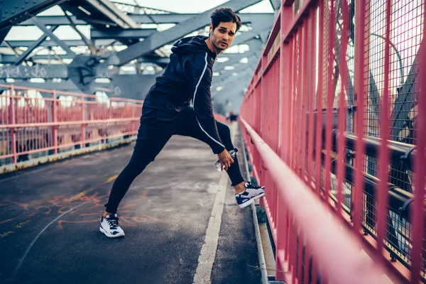 Jovem Homem Flexível Sportswear Alongando Livre Olhando Para Longe Enquanto — Fotografia de Stock