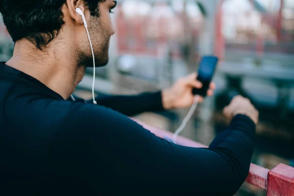 年轻运动员的背部视野在户外训练和寻找新的歌曲为动机 活跃男性运动员收听音乐通过电子耳机和移动应用的小突破 — 图库照片