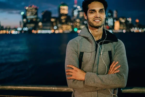 Half length portrait of happy male runner smiling and looking at camera after jogging outdoors and listening positive motivation audio record about healthy lifestyle using electronic headphones