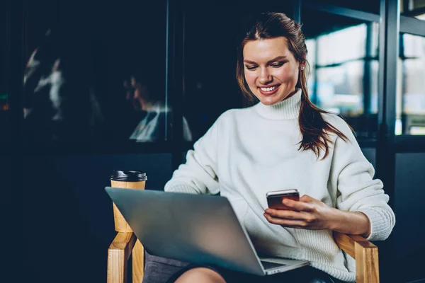 快乐的女性博客通过蓝牙连接通过智能手机和笔记本设备共享信息 微笑着成功的时髦女孩阅读来自朋友在咖啡馆休息的正面电子邮件信息 — 图库照片