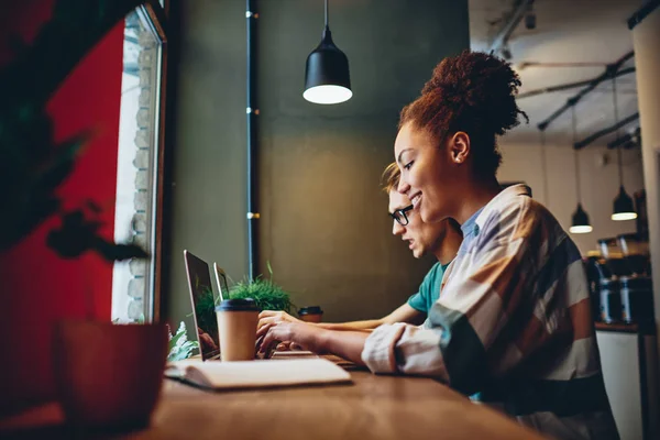 多种族的男性和女性同事在咖啡馆内部远程工作 微笑着黑皮肤的女人在上网本上打字使用应用程序为 学习和研究享受自由时间与朋友 — 图库照片