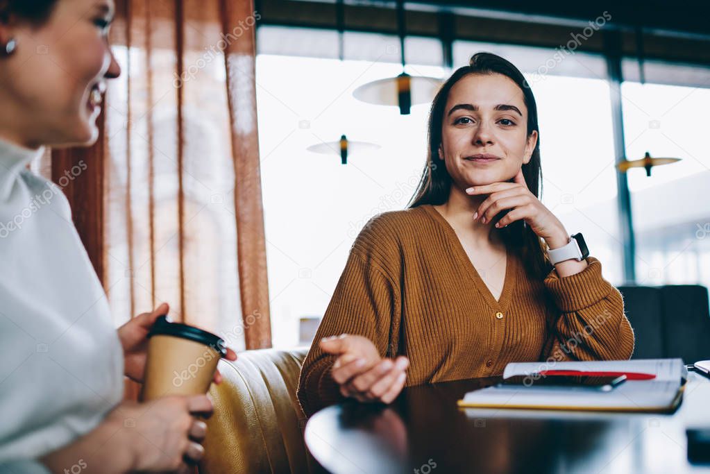 Portrait of attractive hipster girl looking at camera resting with female friend at coffee shop on leisure , gorgeous positive woman sitting at table with textbook for education and planning