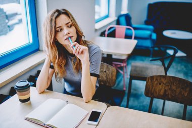 Genç şaşkın kadın yazar vasıl okul sırası ile defter, kalem tutan ve kahve dükkanında makale oluşturmak için vakit zeki şaşkın hippi kız oturan çok satan yeni parçası düşünüyorum