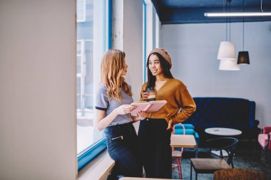 İki mutlu trendy bayan arkadaş birlikte boş vaktinizi ve edebiyat kahve dükkanında Üniversitesi kafeterya, mola sırasında pozitif en çok satan tartışırken genç başarılı hipster girls toplantısı