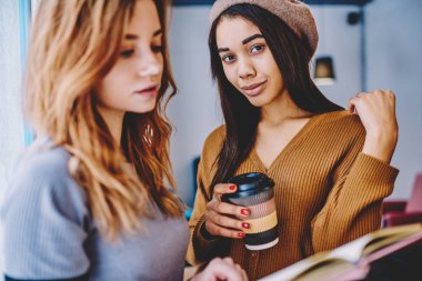 Kameraya bakıyor ve elinde kahve ayakta beyaz arkadaş okuma ilginç bir kitap yakınındaki paket servisi olan restoran fincan, kavramı bilgi eğitim ve Ortaklık Afrika kız öğrencinin portresi