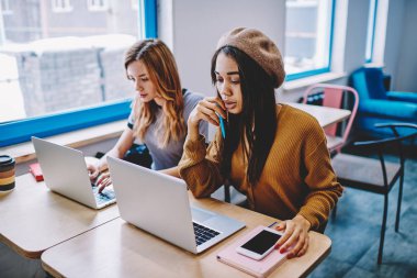 İki ciddi çok kültürlü copywriters birlikte çalışan modern dizüstü bilgisayarlar ve iyi bir internet bağlantısı, kullanarak kampüsünde konsantre kadın serbest webinar üstünde netbook aygıt kapalı bekliyor