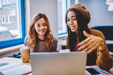 Mutlu çok kültürlü kadınlar birlikte alışveriş online wifi bağlantı başarılı gülümseyen hipster kızlar kahve molası sırasında kapalı netbook olumlu komedi film izlerken laptop aygıt üzerindeki kullanma