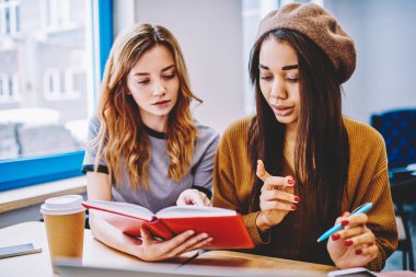 Ciddi istihbarat hipster kızlar, kapalı eğitim için vakit edebiyat okuma iki kız öğrenci bilgi kitap kampüsünde kullanarak başlangıç projesi için araştırma yaparken konsantre