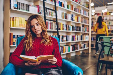 Çekici kız öğrenci yetiştirdim, eğitim, dinlenme Üniversitesi Kütüphanesi'nde zeki çekici hipster kız portresi için ders kitabı tutarak Kitabevi koltukta oturmak için vakit