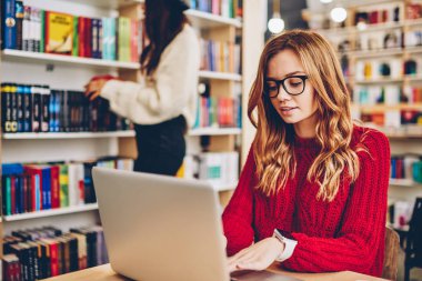 Masaüstü ile modern kitapçı, netbook, çekici kadın iyi bir Internet bağlantısı kullanarak e-posta yazarak gözlük içinde oturmak Web sitesinde yeni yazı için araştırma yaparken konsantre kadın metin yazarı