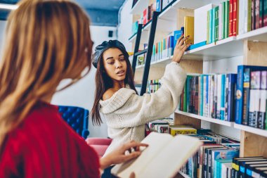 İki zeki kız öğrencilerin araştırma yapmak için okul kütüphanesinde, Genç kadın edebiyat raflardan duran ve eğlence için kapalı en çok satan seçerek genç arkadaş ise okuma projesi.