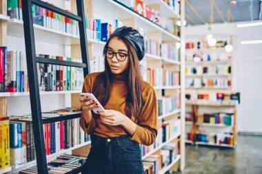 Afrikalı kadın blogger ücretsiz vakit Kitabevi, büyüleyici ve tipik metin haber üstünde hareket eden telefon, Genç hippi kız takipçisi modern cep telefonu üzerinden sosyal ağ e-posta okuma