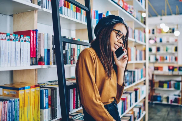 Sorrindo Jovem Hipster Menina Perto Estantes Desfrutar Chamada Celular Amigável — Fotografia de Stock