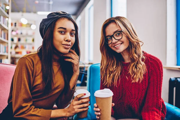 カメラ目線のコーヒー ブレーク 屋内レジャーのキャンパスでテイクアウトのカップを保持しているファッションの女性 代の若者の笑顔幸せを楽しんで成功した多文化流行に敏感な女の子の肖像画 — ストック写真