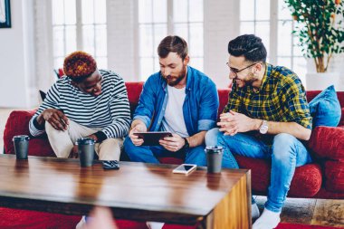 Girintili coworking içinde Wi-Fi bağlantısı ile çok ırklı erkekler modern dijital tablet bilgi aramak için kullanma sosyal ağlardan komik videolar kahve molası sırasında hipster izlemenizi, memnun