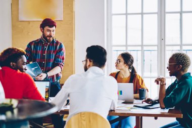 Neşeli erkek çalışan tablo, Toplantı iş arkadaşlarınızla takım için büyük fikirler sunulması ile yetenekli hipster adam iş planı tartışmaya meslektaşlarının çok ırklı ekibiyle bahsediyoruz gülümseyen memnun