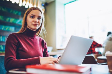 Kafeterya masada, modern bilgisayar ile mesafe iş için alan coworking ve kamera tatilinde bakarak netbook aygıt kullanan beyaz hippi kız oturuyor ve yetenekli kız öğrencinin portresi