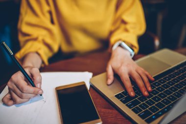 Kurs için kalem yazılı notlarla eller kırpılmış görüntü iş dizüstü bilgisayar, internet içeriği veya Web sitesi için smartphone aygıt ile masada okuyan genç kız öğrencinin kullanan