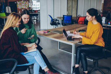 Konuşma sırasında dizüstü bilgisayarla çalışma işlemleri için genç yetenekli neşeli kadın teknoloji ve wifi kullanarak office işbirliği sırasında diğer meslektaşım molada gülümseyen hippi kız orgazm