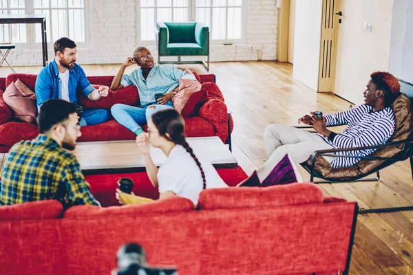 年轻的男性和女性朋友在明亮的现代设计的起居室休闲 一群多种族的同事讨论周末坐在舒适的佛罗里达州红色沙发上的计划 — 图库照片