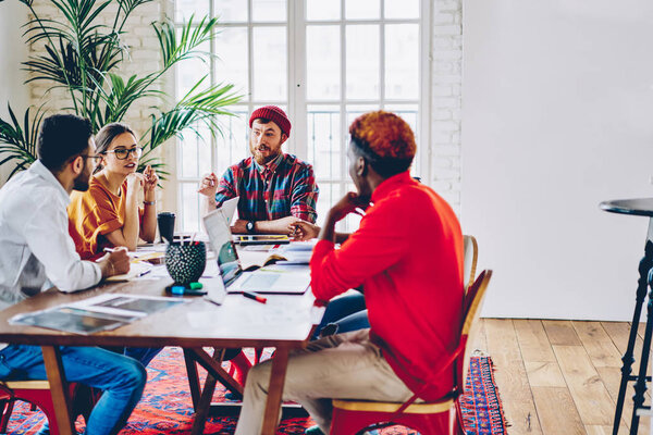 Creative male and female designers having brainstorming session for setting up startup project, leader of working crew discussing ideas cooperating and doing productive job on meeting tabl
