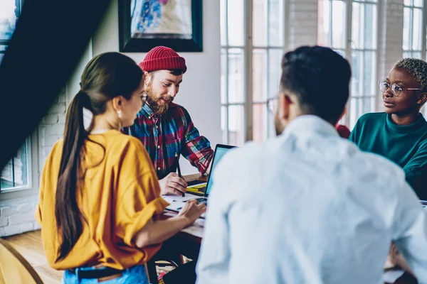 Back view of female and male coworkers sitting at meeting table talking with boss having productive job, crew of multiracial students cooperating on coursework project brainstorming together