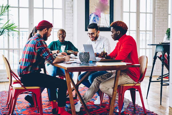 Professional young employees working in team satisfied with process  share ideas and opinions, multiracial crew of designers sitting at meeting table during brainstorming session