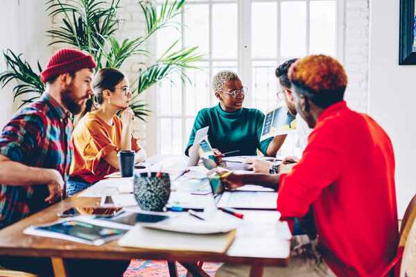 Smart african american female coach of student group checking results of research and speaking on meeting table,serious woman presenting her ideas to multiracial crew 