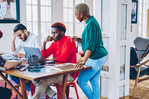 African american female coach helping pensive male student making solution of problem during workshop about business strategies, leader of multiracial working team checking results of productive job