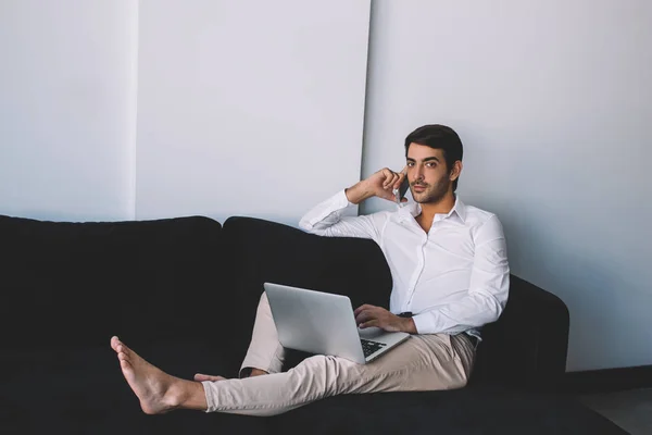 在电话交谈期间 赤脚的时髦的家伙花时间与笔记本电脑休闲 印度男性博客看着相机 而呼吁客户服务通过智能手机 — 图库照片