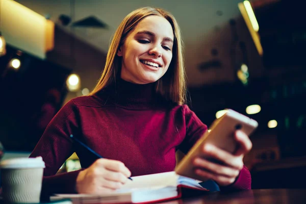 快乐开朗的女人做研究的课程工作 而收到来自朋友的正面短信通过智能手机小工具 微笑的女学生使用互联网上的手机规划行程 — 图库照片