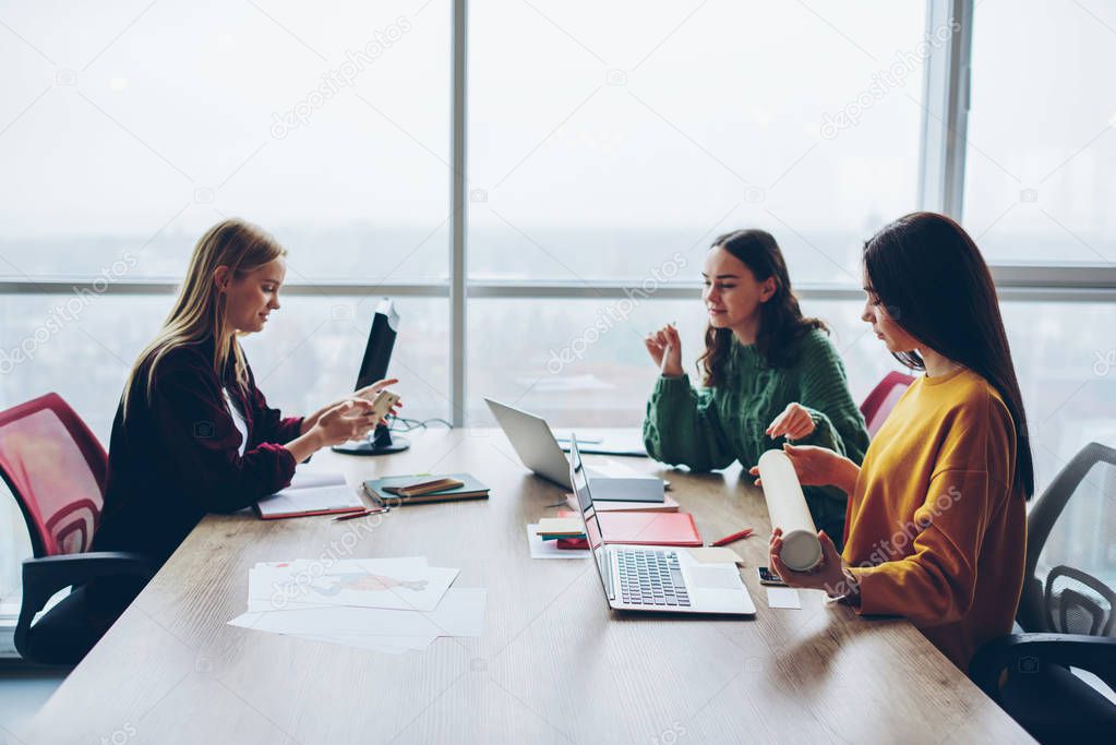 Young women crew of designer having informal meeting for discussing startup ideas together, smart female colleagues communicating at desktop using modern technology and wireless connection in office