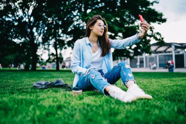 Genç kadın selfie Park'ta serbest zaman sırasında fotoğraf bloglama college Kampüsü boş zamanlarında üzerinde yeniden oluşturmak için cep telefonunda alarak hippi kız oturan smartphone kamera için poz gözlükler