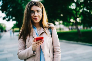 Online rezervasyon için 4 g cep telefonu bağlamadan çekici hippi kız sokakta, ayakta iken smartphone tutan yapma hakkında gözlük düşüncesinde dalgın genç kadın bahar gününde dinlenme internet