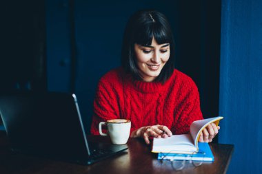Edebiyat kafeterya anda otodidakt için harcama eğitim okuma neşeli hippi kız olumlu kitap ve Masaüstü dizüstü bilgisayar ile oturup kapuçino keyfi bob saç kesimi ile gülümseyen kadın