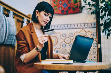 Bohem kafeterya, çekici kadın okuma modern netbook üzerinde işlem yapmak için kredi kartı sayısı, otururken dizüstü bilgisayar yolu ile online alışveriş beyaz hippi kız sevimli