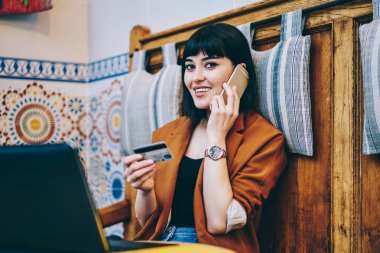 Müşteri Hizmetleri ile konuşmak ve kredi kartı kameraya bakarken elinde tutan neşeli hippi kız portresi, pozitif kadın onaylamak satınalma yolu ile telefon görüşmesi, ödeme ve para kavramı