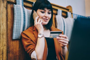 Pozitif kadın numarası kredi kartı arıyor ve kapalı dinlenme sırasında akıllı telefon konuşma ile ödeme yapma hippi kız gülümseyerek Müşteri Hizmetleri telefon üzerinden satın onaylamak