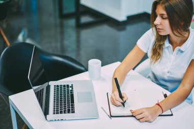 Dalgın yetenekli öğrenci dizüstü online Webinar izliyor ve kablosuz internet bağlantısı kullanarak bir not defteri içinde notlar yapma. Web sayfasındaki bilgileri okuma sırasında Notlar yapma genç kadın konsantre