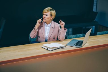 Hayal kırıklığı deneyimli işkadını 50 yaşında modern dizüstü bilgisayarda çalışan akıllı telefon görüşme sırasında ağlıyor. Huysuz kadın profesörü çözme sorun cep üzerinde arama