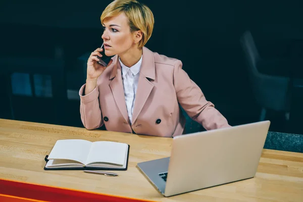 自信的女企业家50岁的时候 在数字上网本设备的工作中交流智能手机 成熟的女商人呼吁现代蜂窝 而看着坐在办公室 — 图库照片