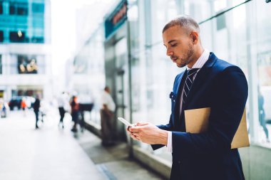 Formal giyim Smartphone cep telefonu ile 4 g internet bağlantısı kullanarak online sohbet metin bildirimi yazmaya konsantre genç girişimci giymiş. Bilgi web sitesinde arama klasörü dalgın gurur ceo