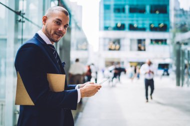 Akıllı telefon tutarak ve 4 g kullanarak App profil güncelleştirme klasörü ile neşeli genç girişimci portresi Internet. Pozitif başarılı iş adamı formal giyim online cep üzerinde sohbet