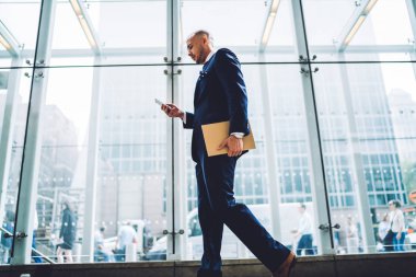 Aşağıda emin girişimci görünümü formal giyim ofis binası içinde gidiş akıllı sms mesajı yazarak giymiş. Gurur ceo 4 g kullanarak modern telefonda App yükleme Internet