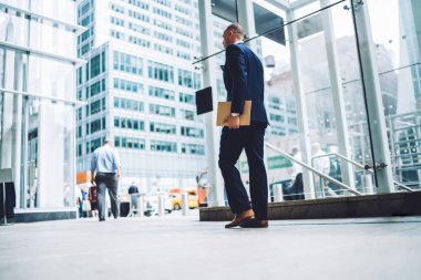 Başarılı iş adamı arkadan görünüm belgeler klasörüyle tutarak ve ofis binası koridorunda gidiş şık takım elbise giymiş. Girişimci formal giyim mali şirket içinde gezinme