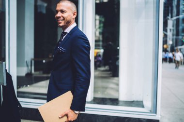 Pozitif işadamı modern şehrin kentsel ortamda gezinme sırasında gülüyor giymiş şık takım elbise giymiş. Başarılı girişimci formal giyim holding klasöründeki gülümseyen ve uzağa arıyorsunuz