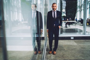 Emin erkek girişimci portresi şık takım elbise kentsel ortamda açık havada duran giyinmiş. Ciddi deneyimli iş adamı cebine elini tutarak ve kameraya bakarak formal giyim
